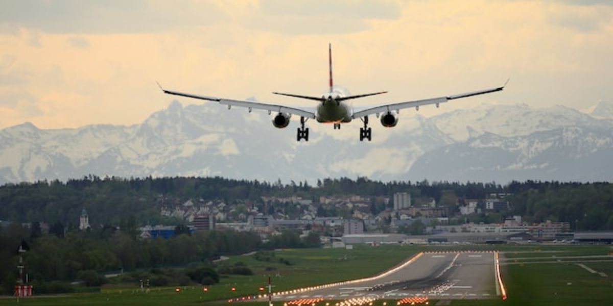 An airplane is taking off from an airport runway with mountains in the background
